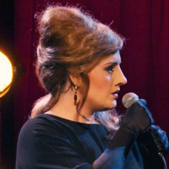 Adele haciéndose pasar por una imitadora suya con nariz y peluca postiza. Adele haciéndose pasar por una imitadora suya con nariz y peluca postiza.