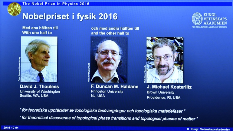 Imagen de una pantalla en la Academia de Ciencias de Estocolmo, Suecia, que muestra a los científicos británicos David Thouless, Duncan Haldane y Michael Kosterlitz.