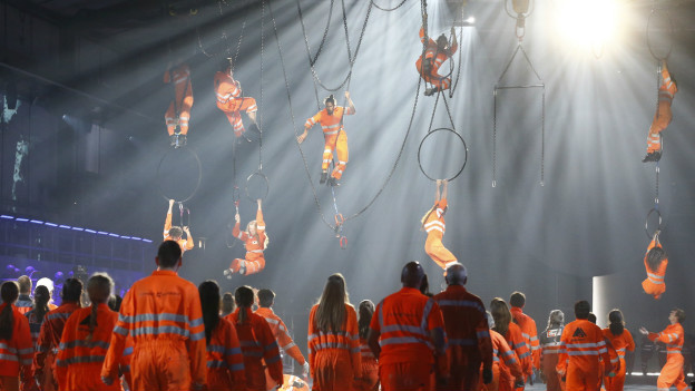En un momento dado, algunos actores semidesnudos rodaban por el escenario. Mientras otros, vestidos como trabajadores de la construcción, se colgaban del techo haciendo piruetas artísticas. En un momento dado, algunos actores semidesnudos rodaban por el escenario. Mientras otros, vestidos como trabajadores de la construcción, se colgaban del techo haciendo piruetas artísticas.