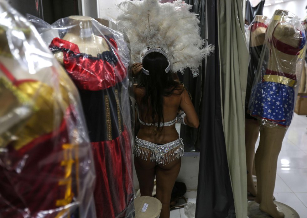 En uno de los probadores de la tienda, Marina, una joven argentina, se prueba un atrevido disfraz cargado de pedrería de colores y un inmenso tocado de plumas en la cabeza. En uno de los probadores de la tienda, Marina, una joven argentina, se prueba un atrevido disfraz cargado de pedrería de colores y un inmenso tocado de plumas en la cabeza.